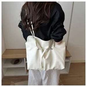 Closeup of a stylish white leather tote bag with belt detail worn by a model in a clean room.