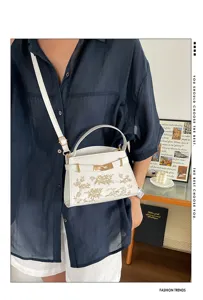 Detail view of a stylish white women handbag featuring elegant gold hardware and floral embroidery.