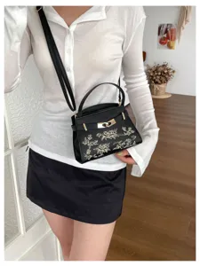 Detailed shot of stylish black top handle shoulder bag with golden floral embroidery for women.
