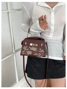 Detail shot of brown women's shoulder handbag featuring exquisite floral embroidery and metal lock.