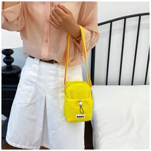 Yellow mini crossbody bag detail view, casual canvas shoulder bag with front pocket design.