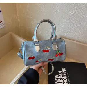 Close-up view of denim Boston handbag featuring cute red cherry embroidery and silver handles.