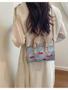 Denim Boston bag detail showing delicate red cherry embroidery and cute pendant accessory.