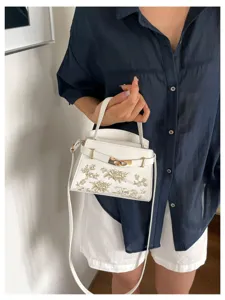 White women handbag with gold hardware, elegant floral embroidery, top handle and strap.
