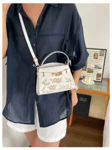 Elegant white leather top handle crossbody bag with gold hardware and chic floral design.