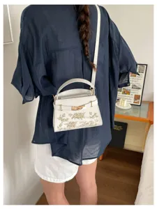 Elegant white leather top-handle crossbody bag with chic gold floral embroidery for women.