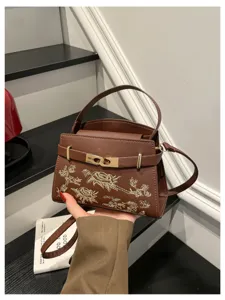 Elegant brown leather handbag for women with exquisite gold embroidery and metallic lock details.