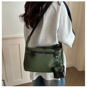 Crossbody bag detail showing green nylon fabric, front zipper pocket and mini hanging pouch.