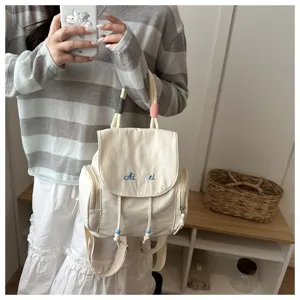 Vista detallada de una mini mochila informal de lona blanca con bordado y cierre de cordón.