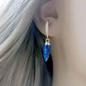 Primo piano dettagliato di orecchini pendenti in pietra blu con cerchio luminoso in zirconi.
