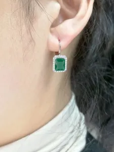 Primo piano dettaglio di orecchini pendenti con pietra verde e cornice di zirconi scintillanti.