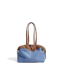 Détail du sac bandoulière en denim avec poignées en cuir marron et fermeture zippée.
