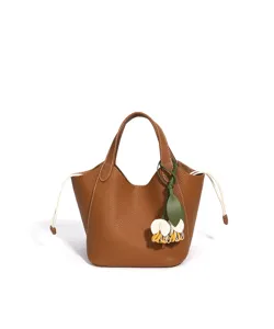 Détail du sac seau en cuir marron avec coutures blanches et charmante fleur.