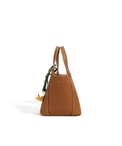 Vue détaillée du sac seau en cuir marron avec coutures exquises et charmant pendentif vert.