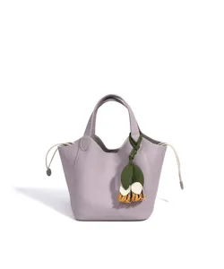 Detail de joli sac seau en cuir lavande avec cordon blanc et charm fleuri vert.