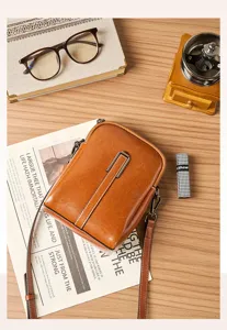 Detailed shot of vintage brown leather phone crossbody bag with metal buckle on retro tabletop.