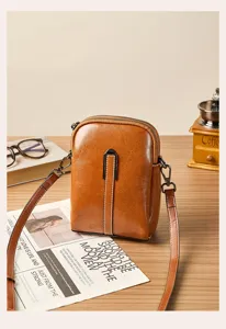 Detail shot of retro brown leather phone crossbody bag with double zippers and metal buckle.