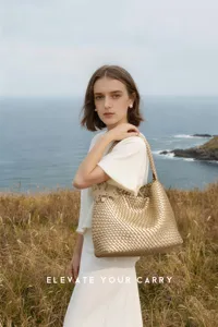 Close-up of the metallic gold woven shoulder handbag in a coastal vacation setting.