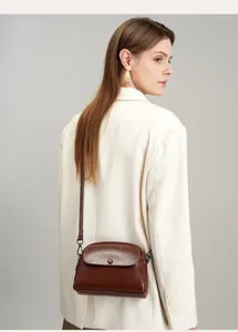 Detail view of a vintage brown leather crossbody bag worn by a model in a white blazer.