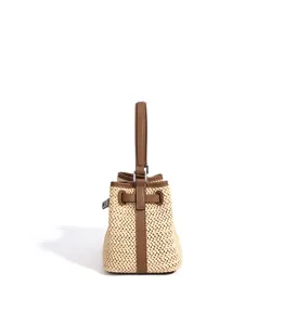 Close-up detail of straw woven bucket bag with brown leather trim and handle for summer vacation.