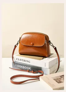 Detail shot of retro brown leather crossbody bag resting on books, elegant fine strap.