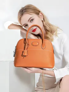 Elegant orange leather dome handbag for women, top handle shoulder bag with lock charm.