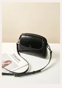Close-up detail of black leather crossbody bag, vintage style with contrast stitching.