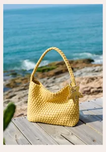 Detailed view of a stylish yellow woven shoulder bag on wooden deck, summer beach style.