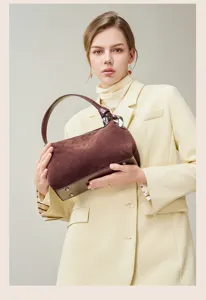 Detail view of a stylish brown suede women handbag held by a model, showing texture.