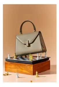 Elegant genuine leather top-handle handbag with trapezoid flap design and metal closure.