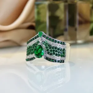 Dettaglio di un ampio anello argentato a forma di corona con zirconi cubici verdi brillanti.