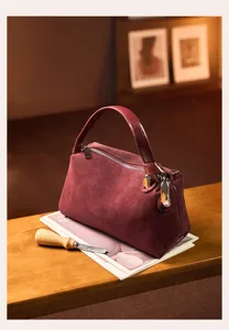 Burgundy suede handbag detail showcasing exquisite zipper closure and metal ring handle design.