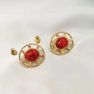 Primo piano di orecchini a lobo rotondi dorati vintage con pietre rosse e chiusure.
