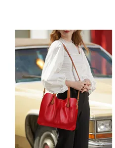 Detail view of red leather women tote bag with brown handles and shoulder strap in vintage setting.