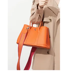 Close-up detail of premium orange leather tote bag with wide strap and elegant metal clasp.
