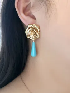 Dettaglio in primo piano di orecchini pendenti con fiore di rosa dorata stile vintage.