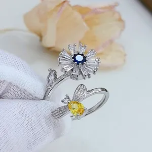 Primo piano dettaglio di anello aperto in argento con fiori e api in zirconi brillanti.
