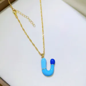 Dettaglio di una collana con ciondolo lettera capsula stile dopamina color oro chic.