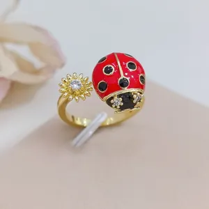 Primo piano dettagliato dell'anello aperto dorato con coccinella smaltata rossa e fiore.
