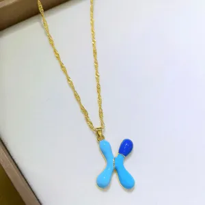 Primo piano dettaglio di una collana catena dorata con ciondolo lettera X smalto blu.