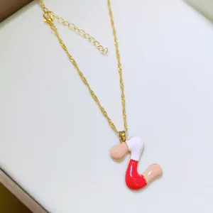 Inquadratura di dettaglio di una collana a catena dorata con ciondolo a lettere smaltate.