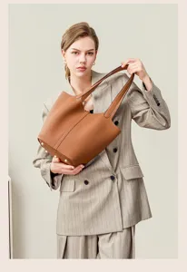 Detailed shot of a brown genuine leather bucket tote bag held by a model in a pinstriped suit.