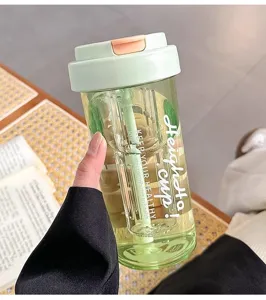 Close-up detail of the clear green plastic water bottle with straw and printed slogan.