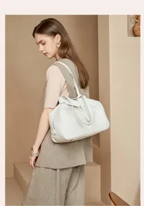 Detailed shot of elegant white leather boston shoulder bag in modern architectural setting.