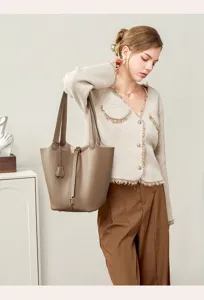 Detail shot of taupe leather bucket bag with lock closure and top handles for women.