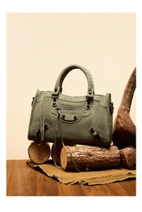 Detailed shot of olive green suede motorcycle handbag with metal studs and tassel.