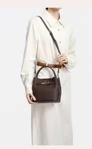 Brown leather bucket bag with top handle and metal lock worn by model, chic everyday handbag.
