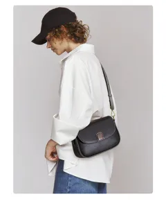 Detail view of black leather crossbody bag worn by model, showing flap design and texture.