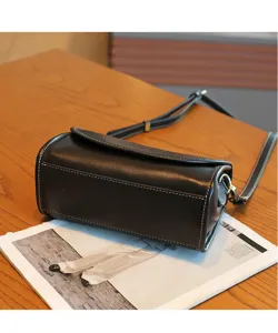 Black leather cylindrical shoulder bag detail, vintage crossbody bag with contrast white stitching.