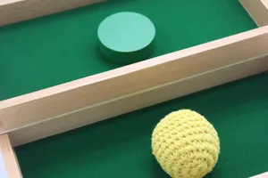 Detail de jouet d'eveil en bois avec disque vert et balle en fil jaune dans le plateau trieur.